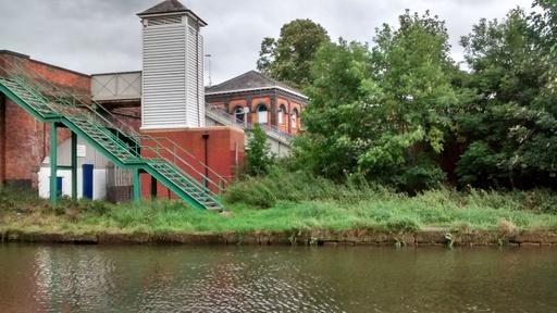 Brooklands Station viewed from the towpath of the Bridgewater Canal. Samuel Brooks negotiated terms for a station in 1859. The building of the station was contracted to John Brogden & Sons.